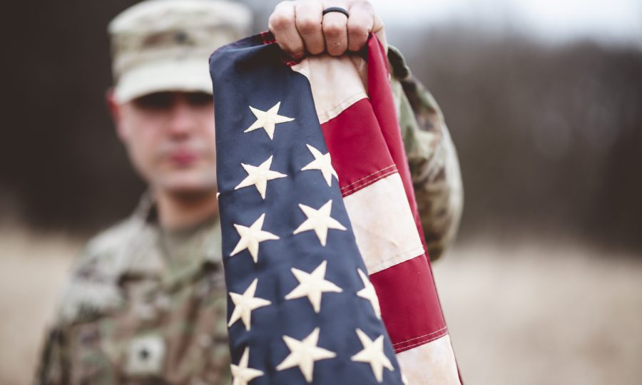 selective-focus-shot-american-soldier-holding-american-flag-close-camera